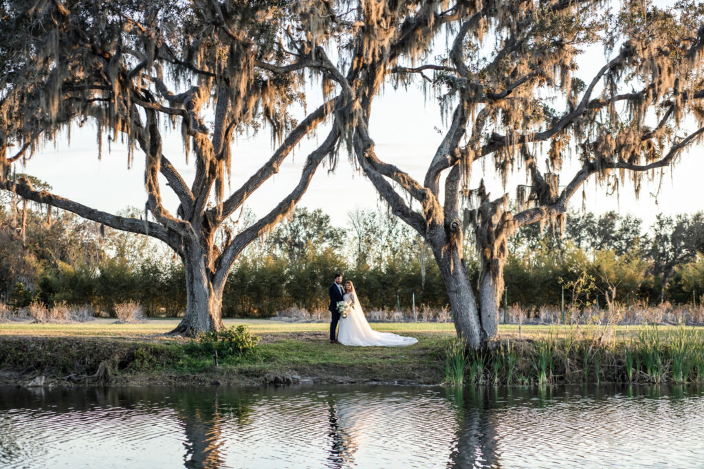 bride and groom standing between two big trees with a lake in front of them