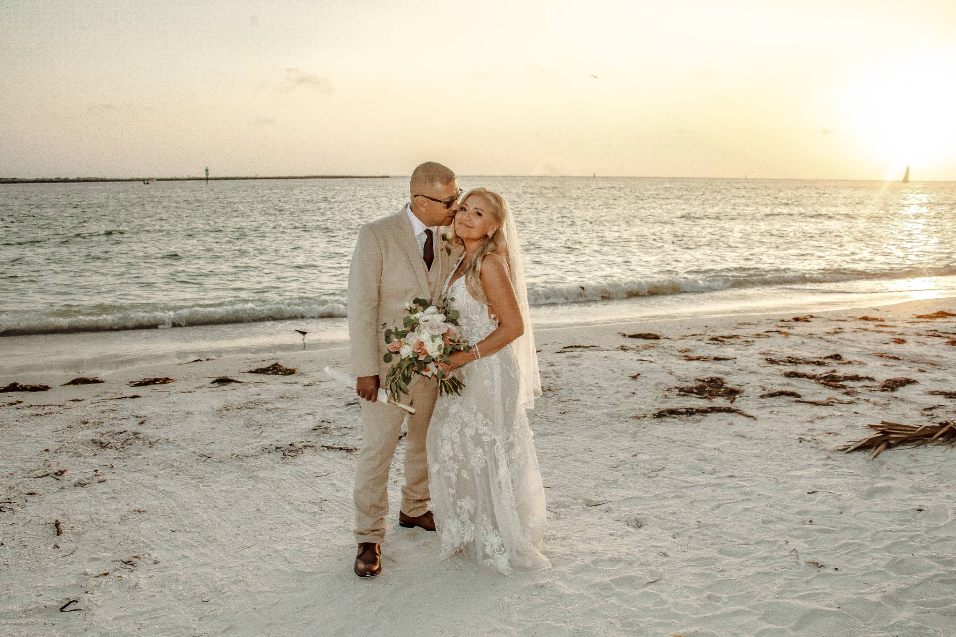 groom kissing bride on the cheek on the beach at sunset